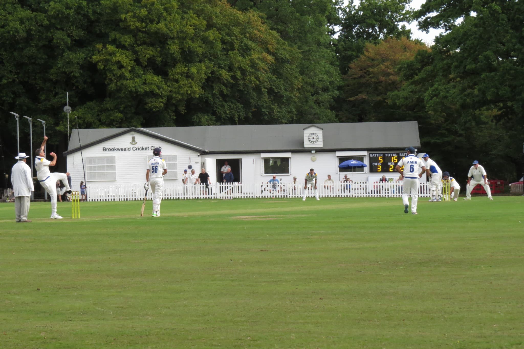 A Brookweald bowler runs in during a league match, with the white clubhouse and scoreboard behind, at Weald Road, Brentwood